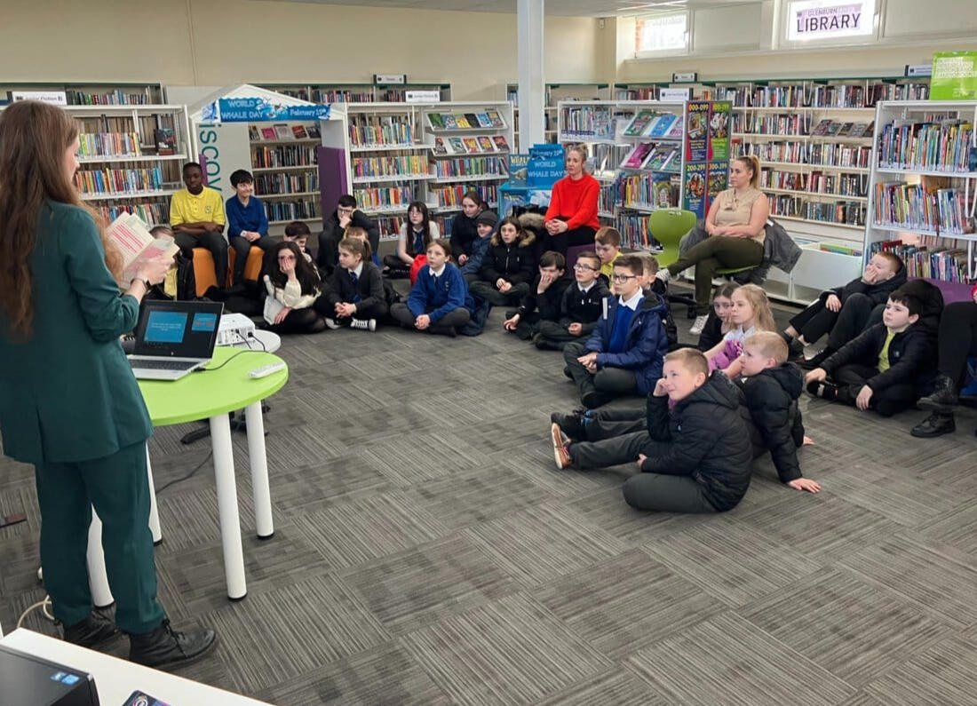 Fiona is standing in a library reading a copy of Looking for Emily to a group of young children.